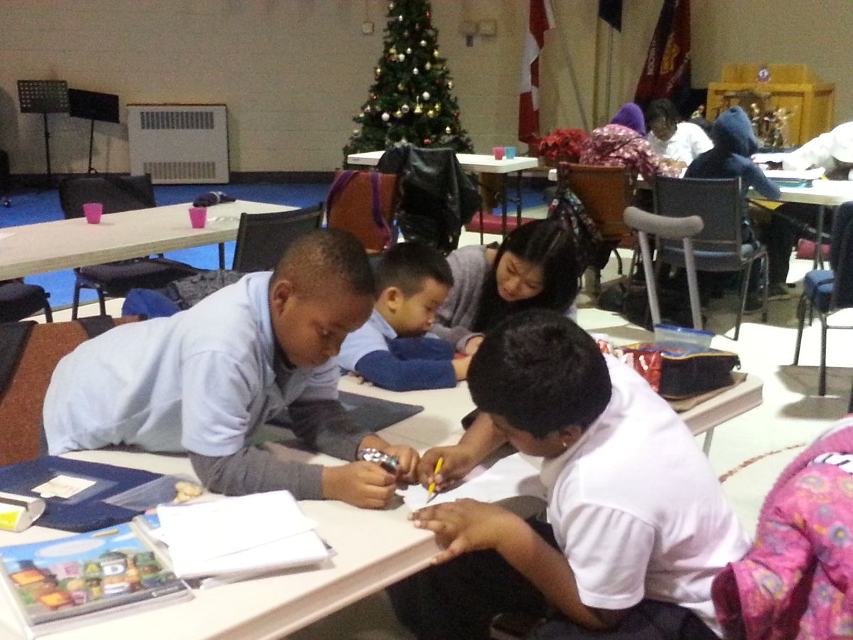 several boys doing homework on a table with the help of a leader